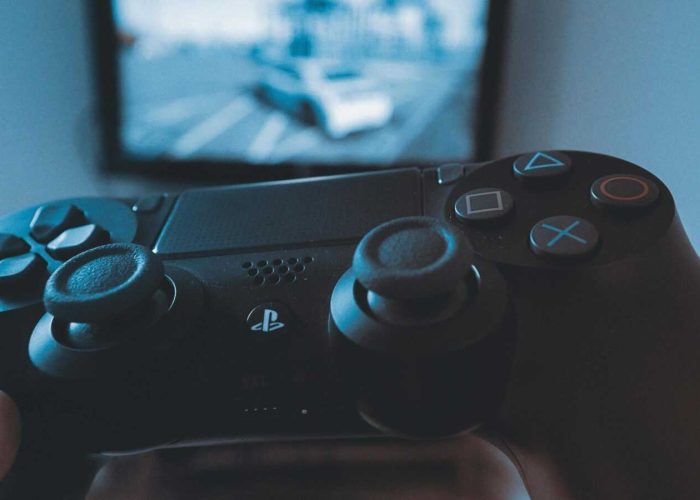A hand holding a wireless game controller in front of a blurry screen, capturing the gaming experience.
